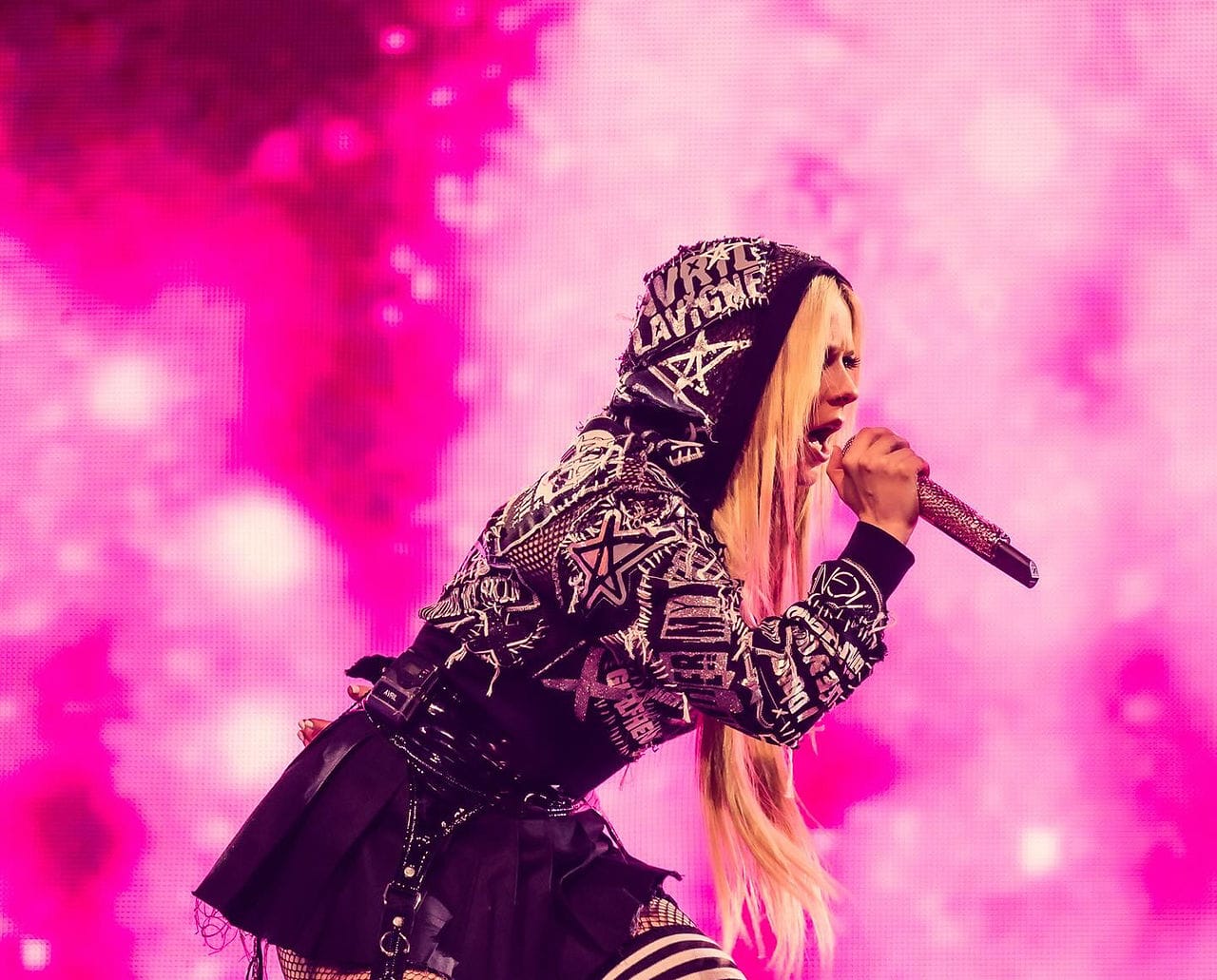 Avril Lavigne на сцене в розовом свете, в толстовке с собственным именем