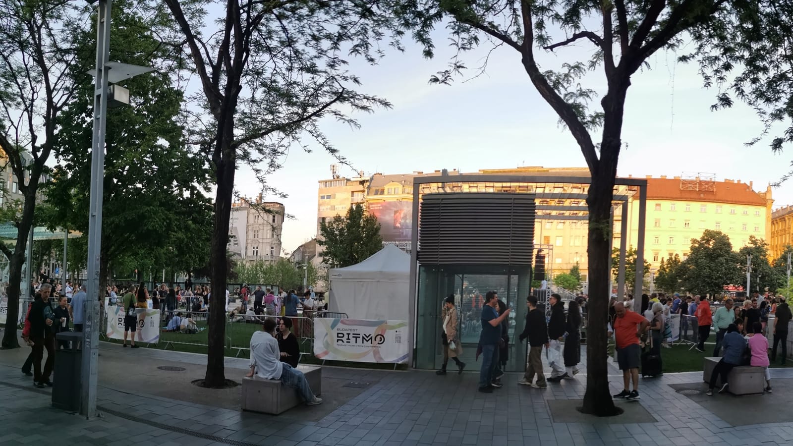 Площадь на Budapest Ritmo 2024: публика между деревьями на закате, вывеска RITMO