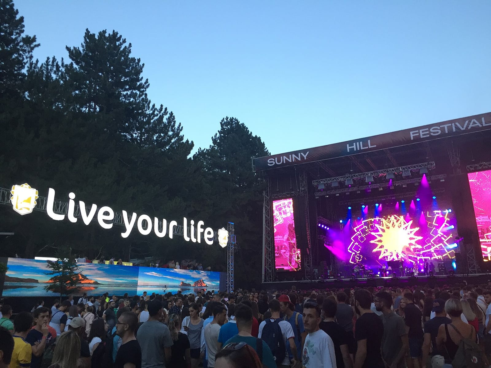 Сцена Sunny Hill Festival в сумерках, толпа и надпись Live your life